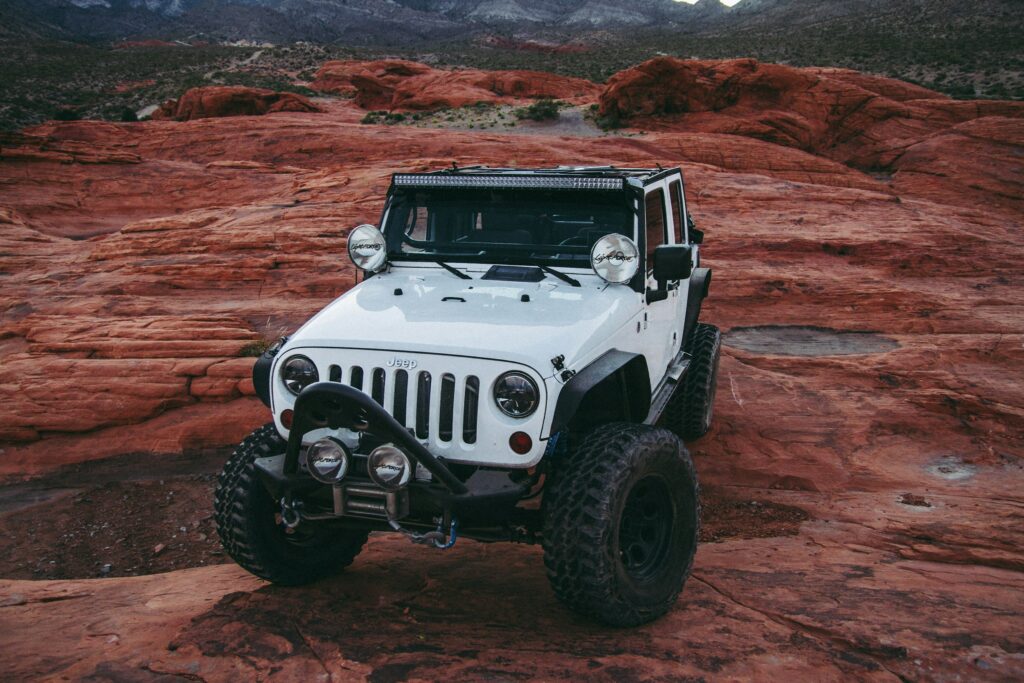 White Jeep Wrangler parked on red sandstone formations in a desert canyon (front view).