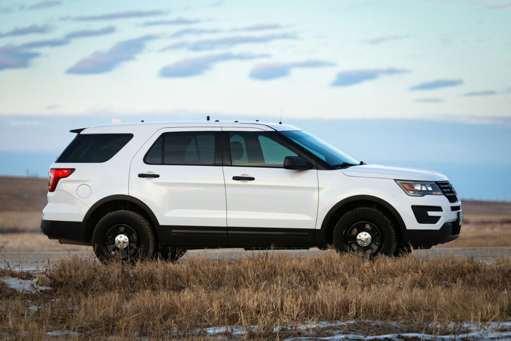 Side view of a white SUV parked on a grassy plain with a blue sky and few clouds.