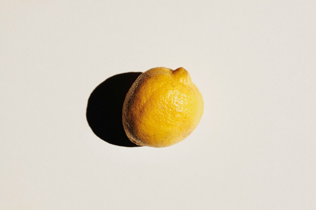 Close-up of a yellow lemon at the bottom-right on a pale background, with a deep shadow to the left.