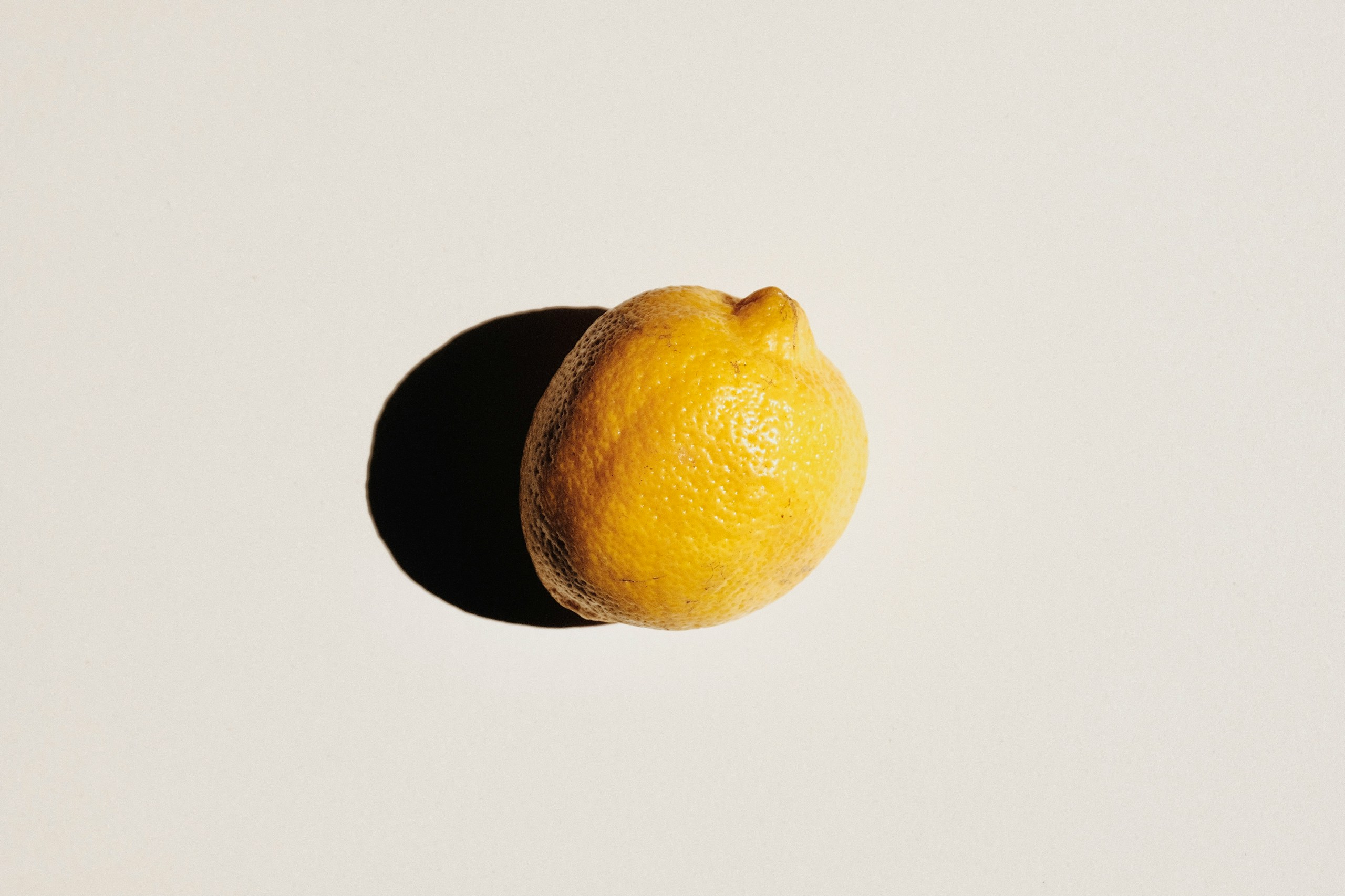 Close-up of a yellow lemon at the bottom-right on a pale background, with a deep shadow to the left.