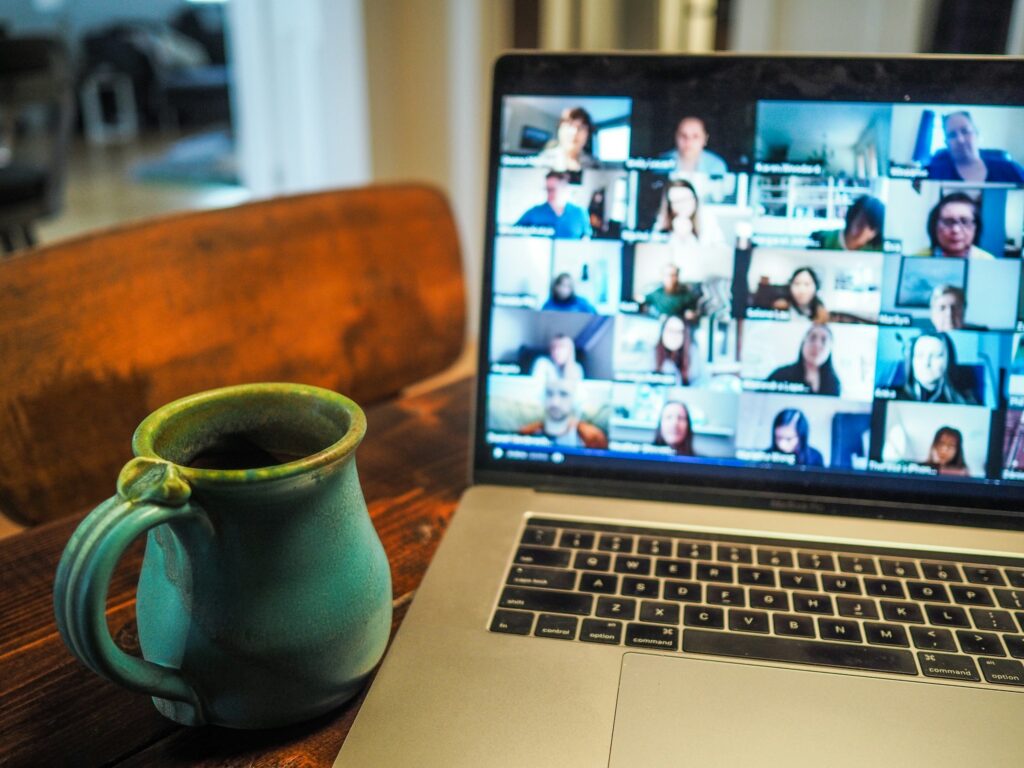 Teal ceramic mug on a wooden table in front of a laptop showing a video conference grid of participants.